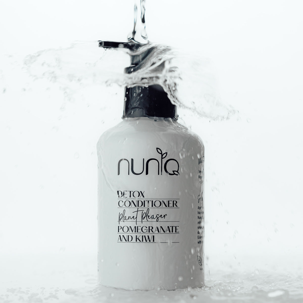 Bottle of Nuniq Detox Conditioner with water being poured over it on a white background