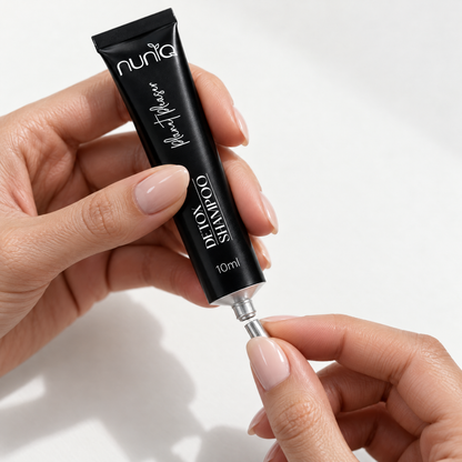 A close-up of hands holding a black squeeze tube of Nuniq Detox Shampoo, with the silver cap snap-off, against a clean white background.